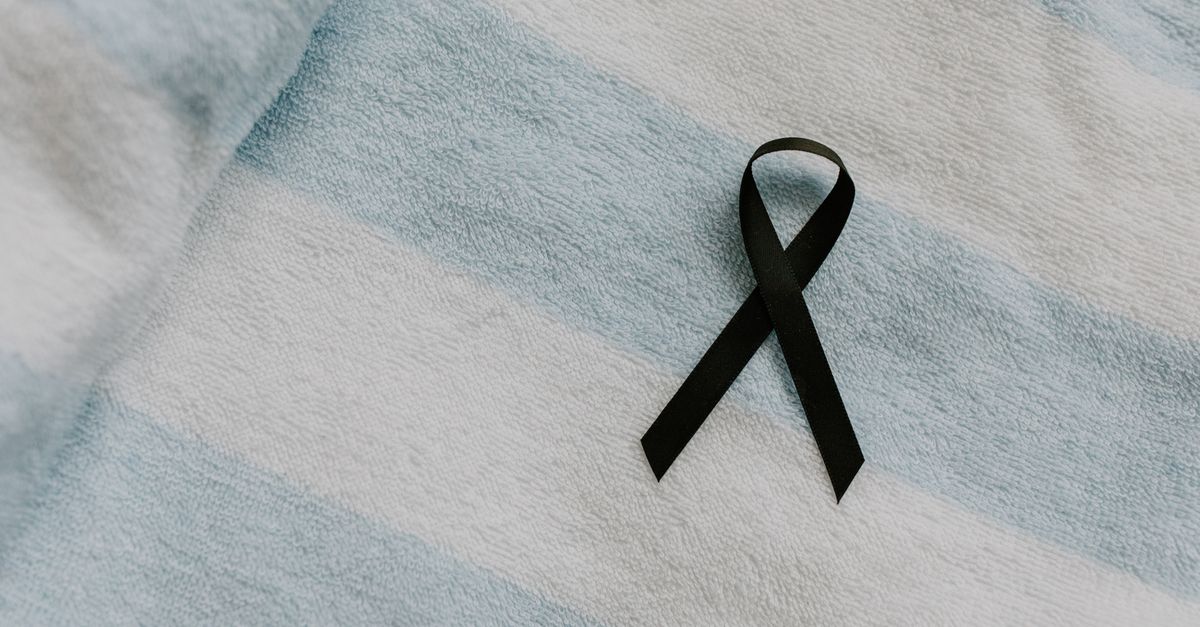 Black awareness ribbon placed on soft, striped fabric symbolizing support and remembrance.